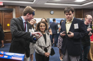 Gus Smith, left, demonstrates his visual assistance smart glove to France Cordova, NSF Director. Peter Zientra, right, looks on.