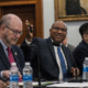 Professor Jenkins, middle, gestures toward his slides during his remarks. Dr. Reed sits to his right and Dr. Song sits to his left.